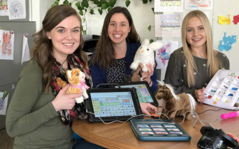 Three speech language pathology students holding augmentative and alternative communication devices