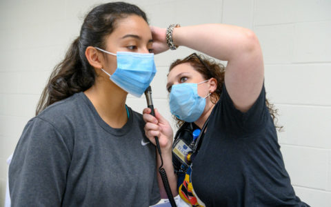 A family nurse practitioner student examining the ear of a high school student