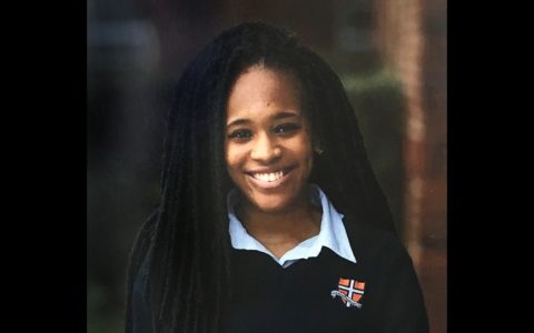 Pamela Okaro smiling and wearing an open-collar blue shirt and a black sweater