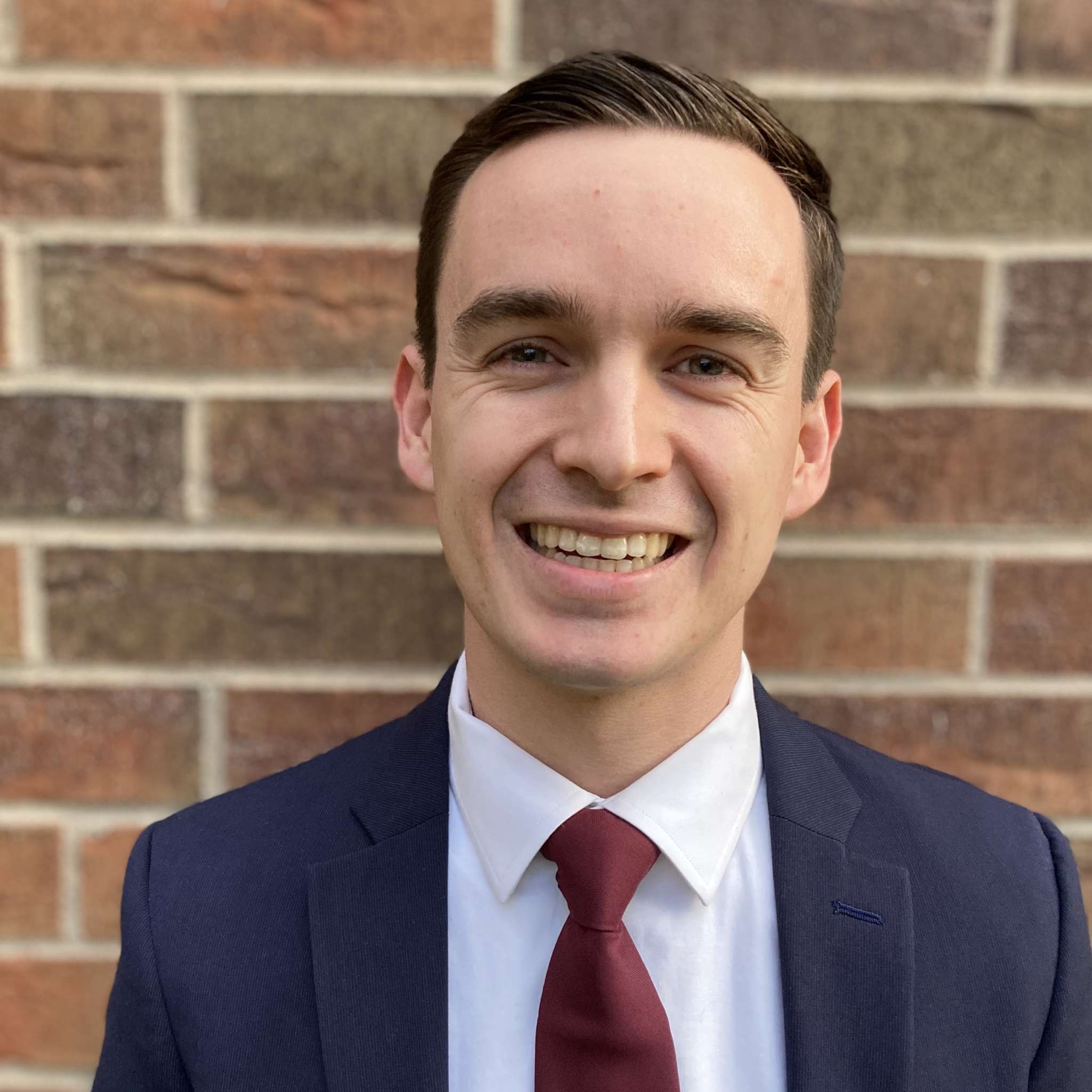 Matthew Cecconi smiling and wearing a white shirt, crimson tie and blue blazer