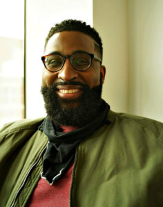 African American man smiling with a beard, glasses and green jacket