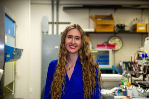 blonde woman with long hair wearing a blue blouse and smiling