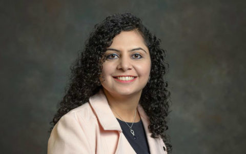 woman with long dark hair wearing a black top and a pink coat