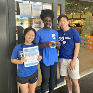 Three people in blue t-shirts standing outside a grocery store