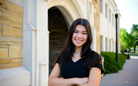 young woman with long dark hair and arms crossed standing outdoors