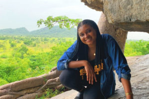 woman with long black hair crouching near a rock formation