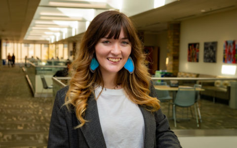 woman with long hair and blue earrings standing indoors and smiling