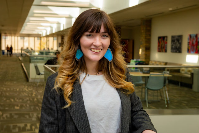 woman with long hair and blue earrings standing indoors and smiling