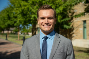 young man with short hair wearing a blue shirt, blue tie and a grey suit jacket