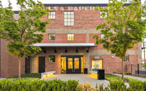 Old red brick three-story building with an illuminated entryway and the partial words Tulsa Paper painted near the top