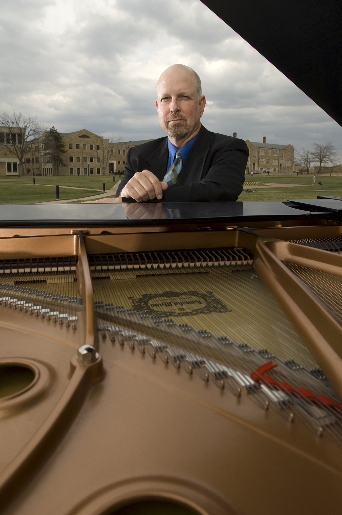 Professor Roger Price sits poses for a photo behind an open-top piano