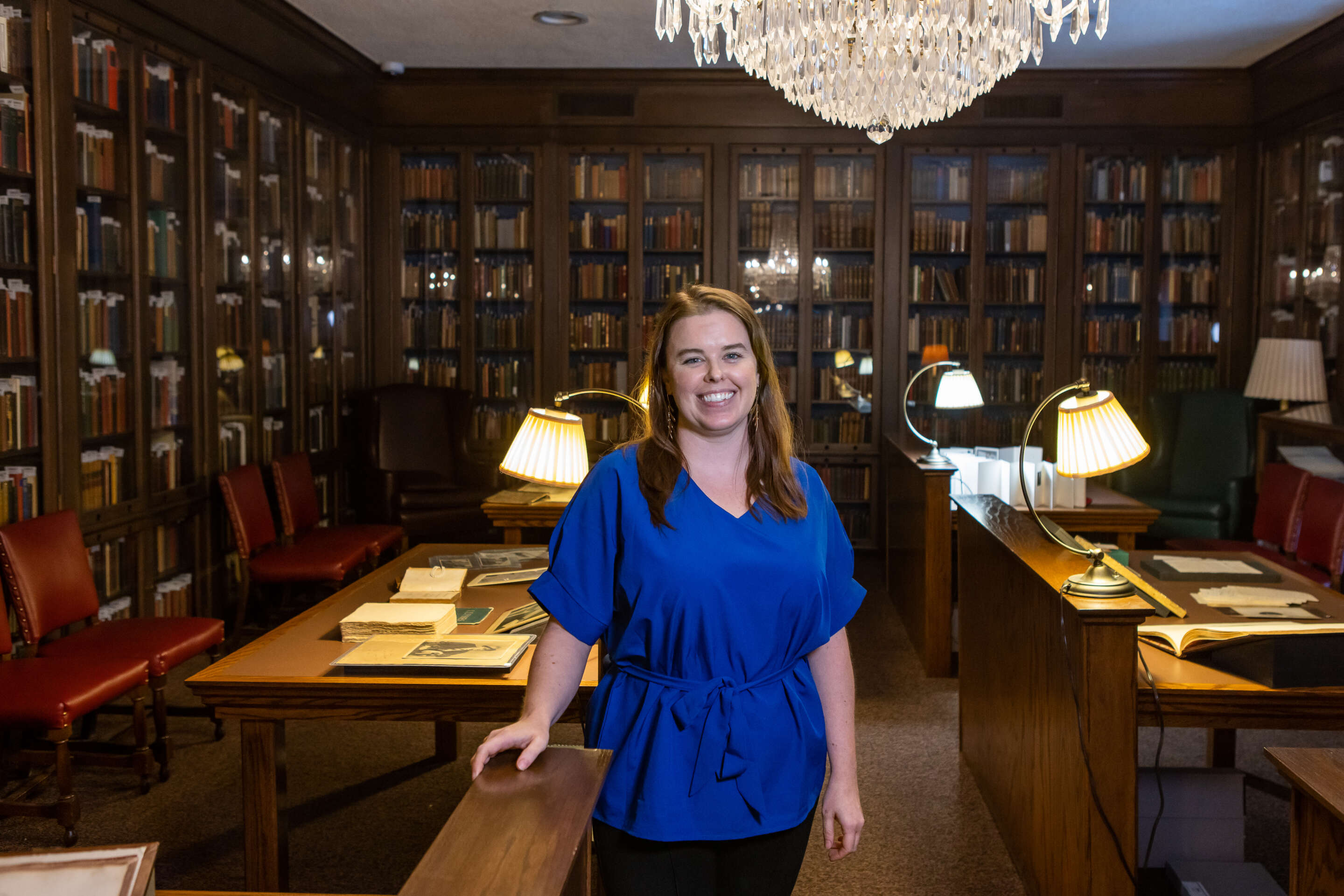 Woman standing in a library wearing a blue shirt smiling for a photo