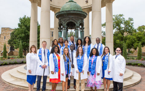 People in lab coats standing in front of bell