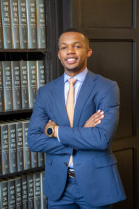 law student in front of a book case with arms folded