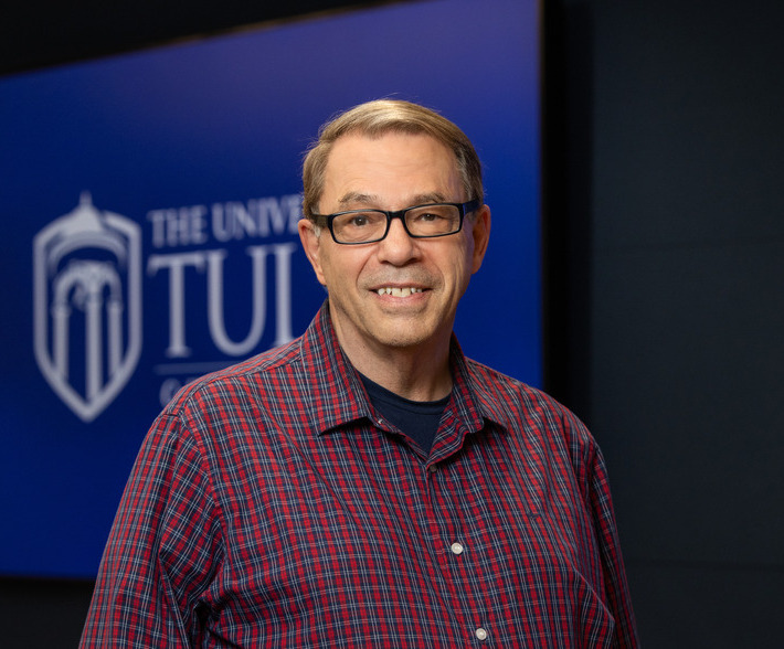 Photo of Wray Bradley smiling in black glasses inside of building.