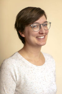 woman with short hair and glasses smiling and wearing a white top