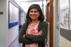 woman standing in a corridor with her arms crossed while smiling and wearing a green cardigan