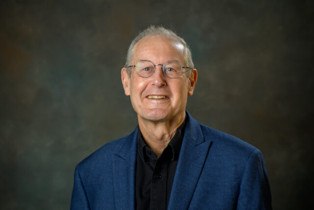 man with short grey hair, glasses and a blue jacket