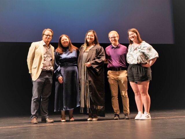 five people standing closely side by side on a stage