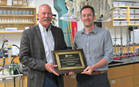 two men standing in a chemistry lab while holding an award plaque