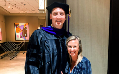 tall man in graduation robe being hugged by a shorter woman