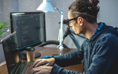 young man seated at a desk in front of two computer monitors