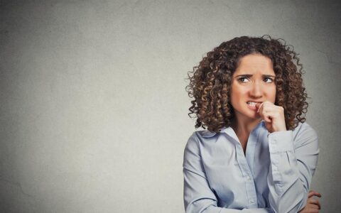 woman with curly hair looking anxious and biting her thumb