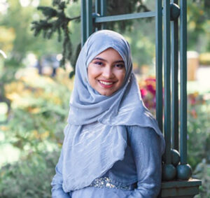 Maliha Maisha smiling and wearing a blue headscarf and dress