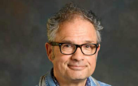 Man with grey hair and glasses wearing a blue shirt