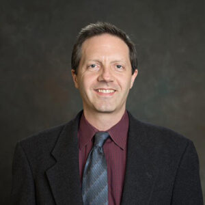 Professor Robert Jackson wearing a maroon shirt, dark tie and black blazer