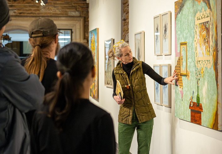 Photograph of a person lecturing a group of students about an artwork displayed in a gallery