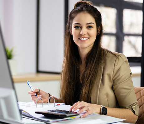 Photograph of a smiling woman using a calculator and making handwritten notes in a binder