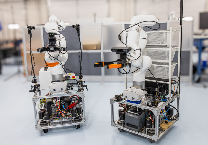 Two mobile robots with robotic arms, part of the Institute for Robotics & Autonomy (IRA) research.