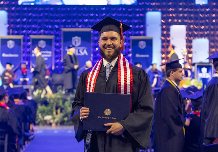 UTulsa student veteran smiling at graduation, holding diploma. #UTulsa jumps in rankings.