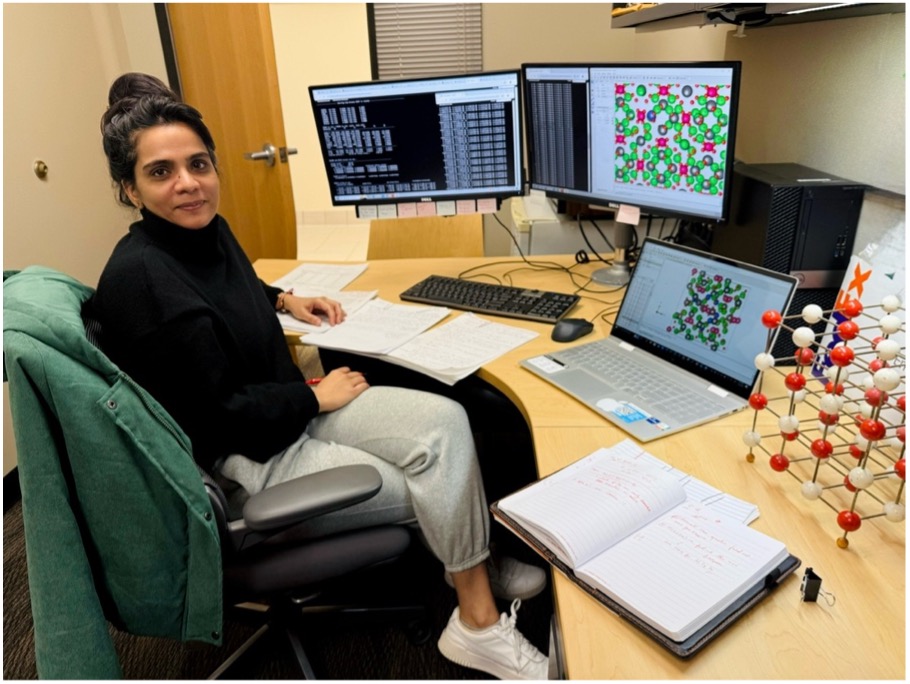 Physics doctoral student at UTulsa working on battery research, surrounded by monitors, a laptop, and scientific models.