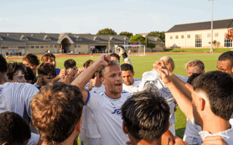 Soccer team huddle with coach, possibly discussing sports leadership program strategies.
