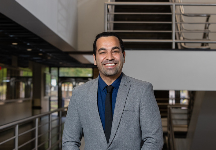 Man in suit smiles in front of stairs. U.S. Army backs university project.