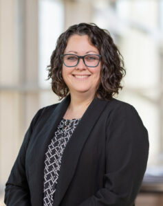 OCII team member Bridget Kurr with glasses and a black blazer smiling at the camera. 