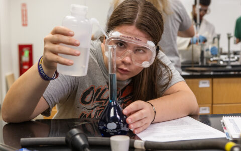 UTulsa student in lab wearing safety goggles, working with blue liquid.