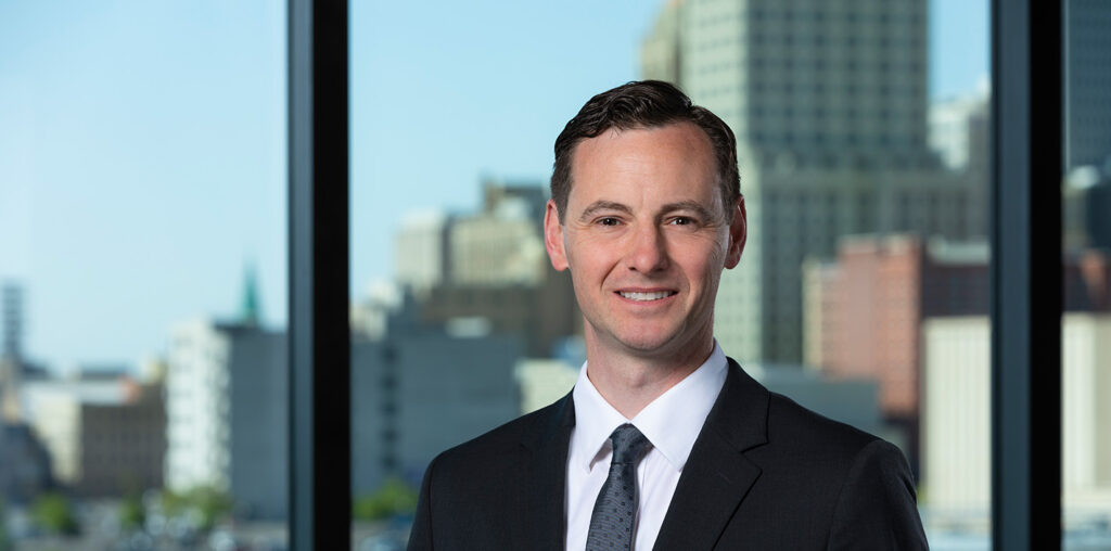 Professional headshot of UTulsa alumnus in suit, city skyline background.