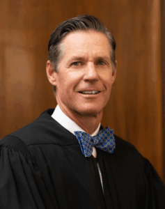 Headshot of Judge Gregory K. Frizzell in judicial robes and a blue bow tie. 