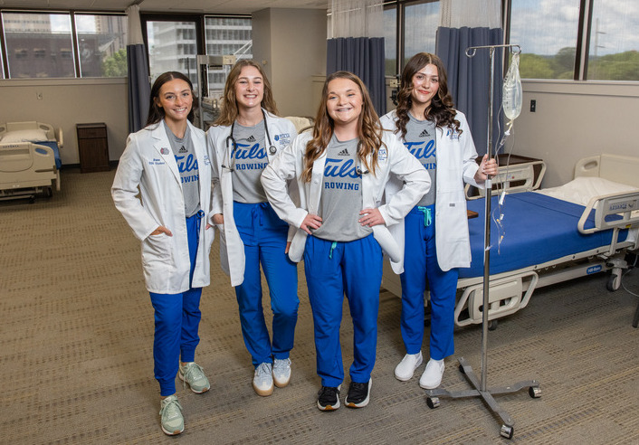 UTulsa nursing students in scrubs and lab coats pose in a hospital training room.