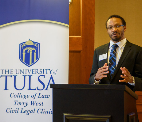 Man speaking at University of Tulsa College of Law event. Terry West Civil Legal Clinic banner visible.