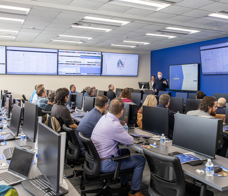 Group of people in a training room with computer monitors and large display screens.