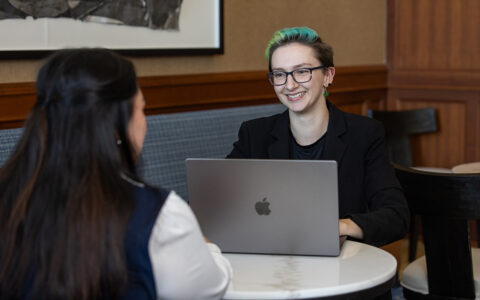 UTulsa MBA student smiling while working on a laptop during a meeting.
