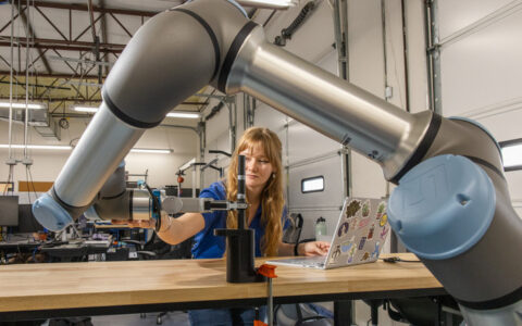 Electrical engineering student working with a robotic arm and laptop in a lab setting.