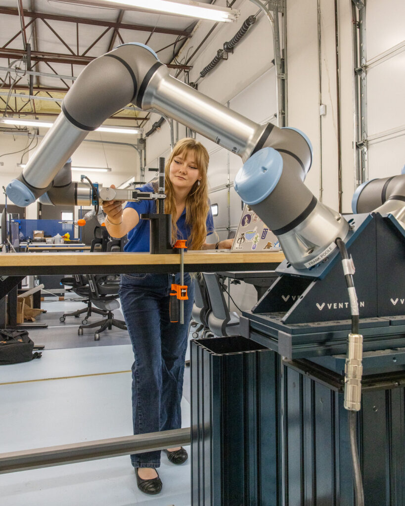 Electrical engineering student working with a robotic arm in a lab setting.
