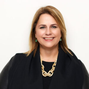 Headshot of a smiling woman in a black jacket and gold necklace. 