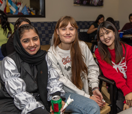 Three smiling students from diverse backgrounds at a global engagement event.