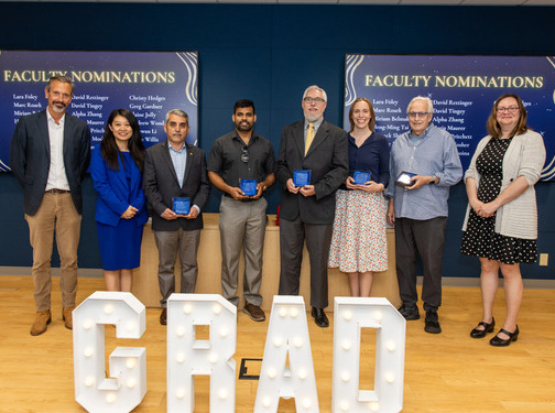 Group of award recipients in front of "GRAD" sign, faculty nominations visible.